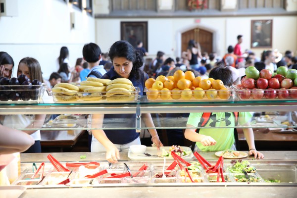 At Burwash Dining Hall, a cafeteria station is depicted, with a teenage girl and boy in line, anticipating their food selection. 