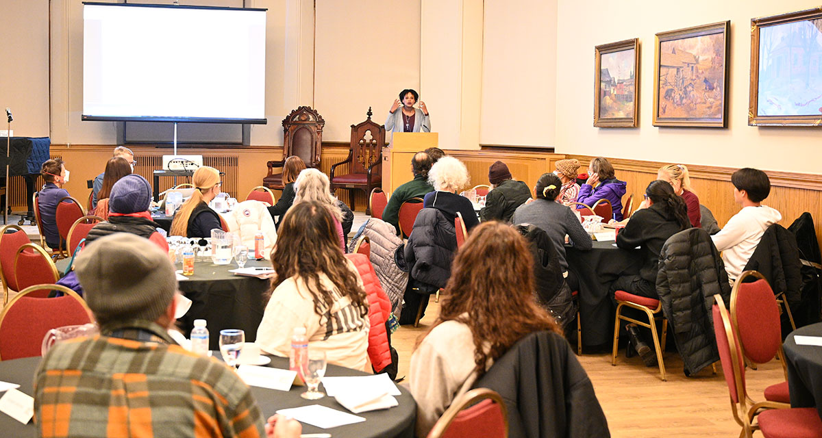 Captivating scene in Alumni Hall as Humanities for Humanity attendees sit at tables, absorbed in the discussion led by speaker Rhonda McEwen at the podium.